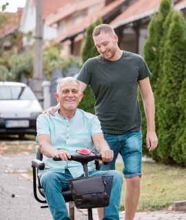 Man in wheelchair outside with man standing next to him, both smiling